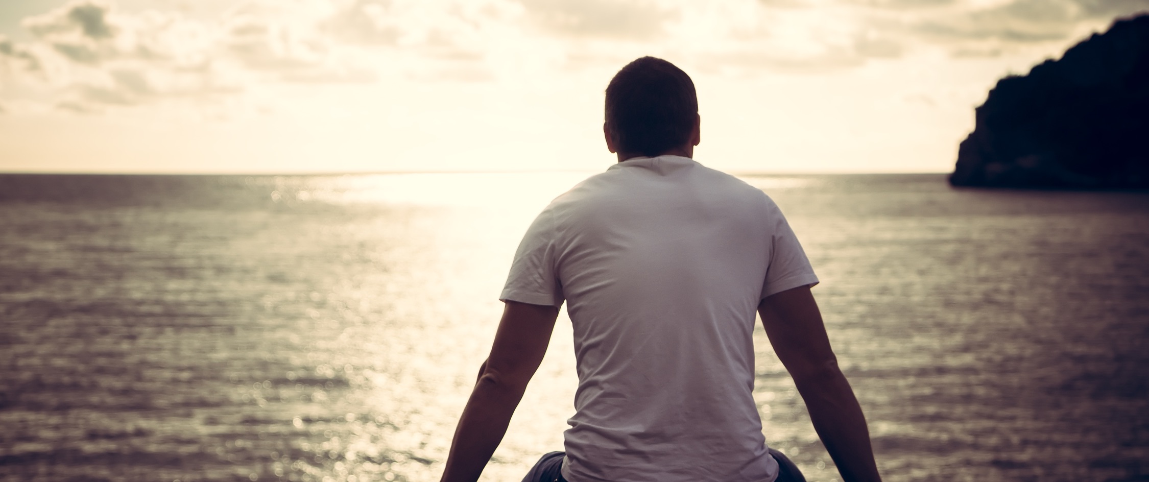 Lonely man looking with hope at the horizon with sunlight during sunset with effect of light at the end of a tunnel.