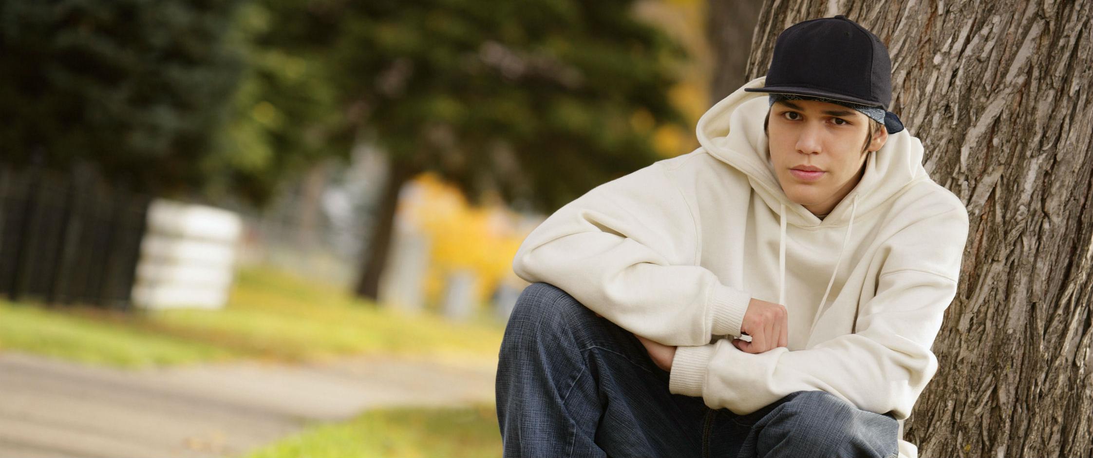 Male youth crouching next to a tree.