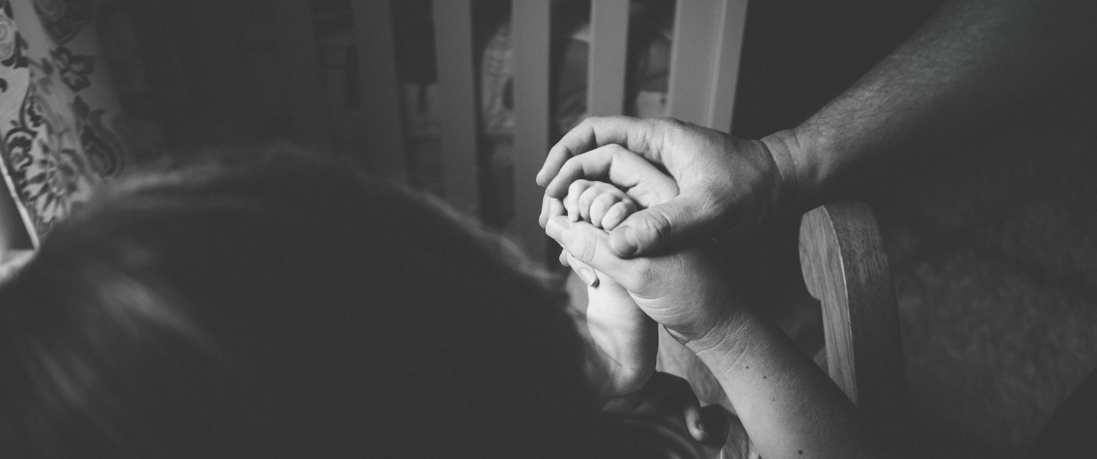 A child's hand being clasped by the hands of adults