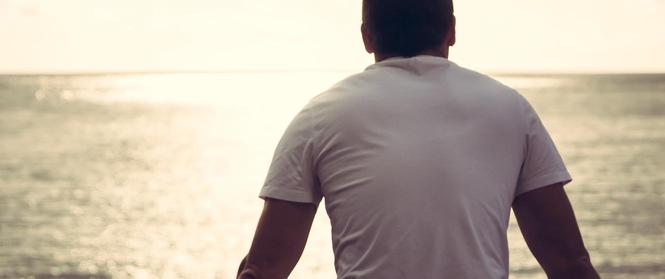 Lonely man looking with hope at the horizon with sunlight during sunset with effect of light at the end of a tunnel.